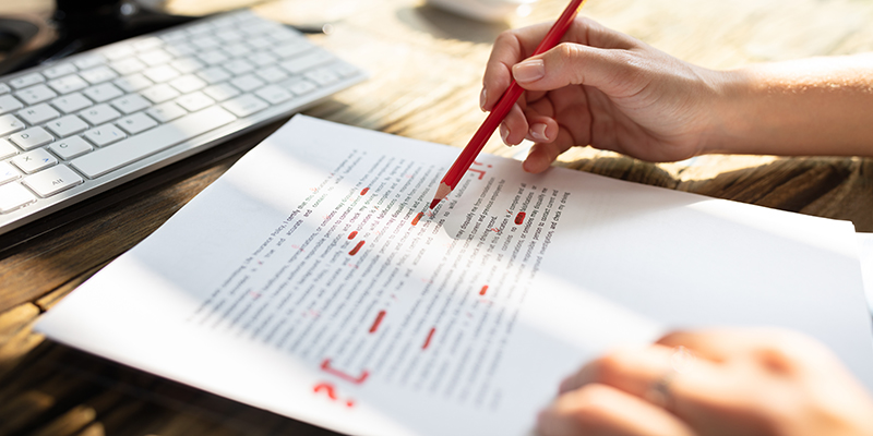 転載イメージClose-up Of A Person's Hand Marking Error With Red Marker On Document