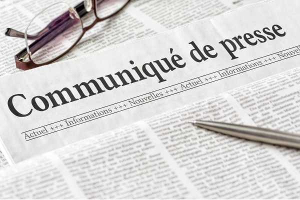French newspaper featuring the headline 'Communiqué de presse', with reading glasses and a pen nearby.