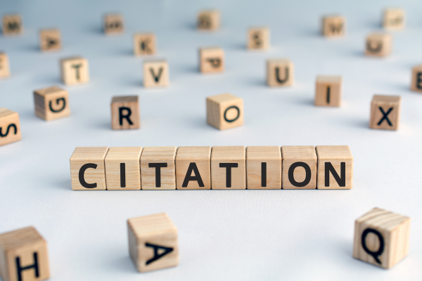 Wooden letter blocks spell 'CITATION' on a light surface with scattered letters in the background.サイテーションと書かれたブロック