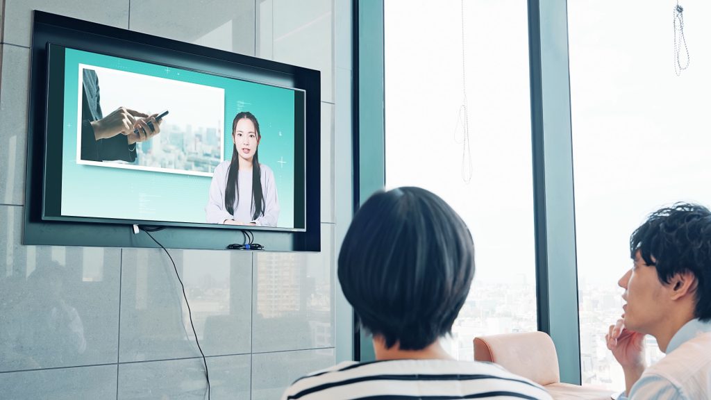 Team watching a presentation on a wall-mounted screen in a modern office, city skyline visible outside the windows.