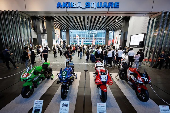 アキバ・スクエア入口に並ぶ4台のレース用バイクと、会場内の展示やステージに集まる来場者