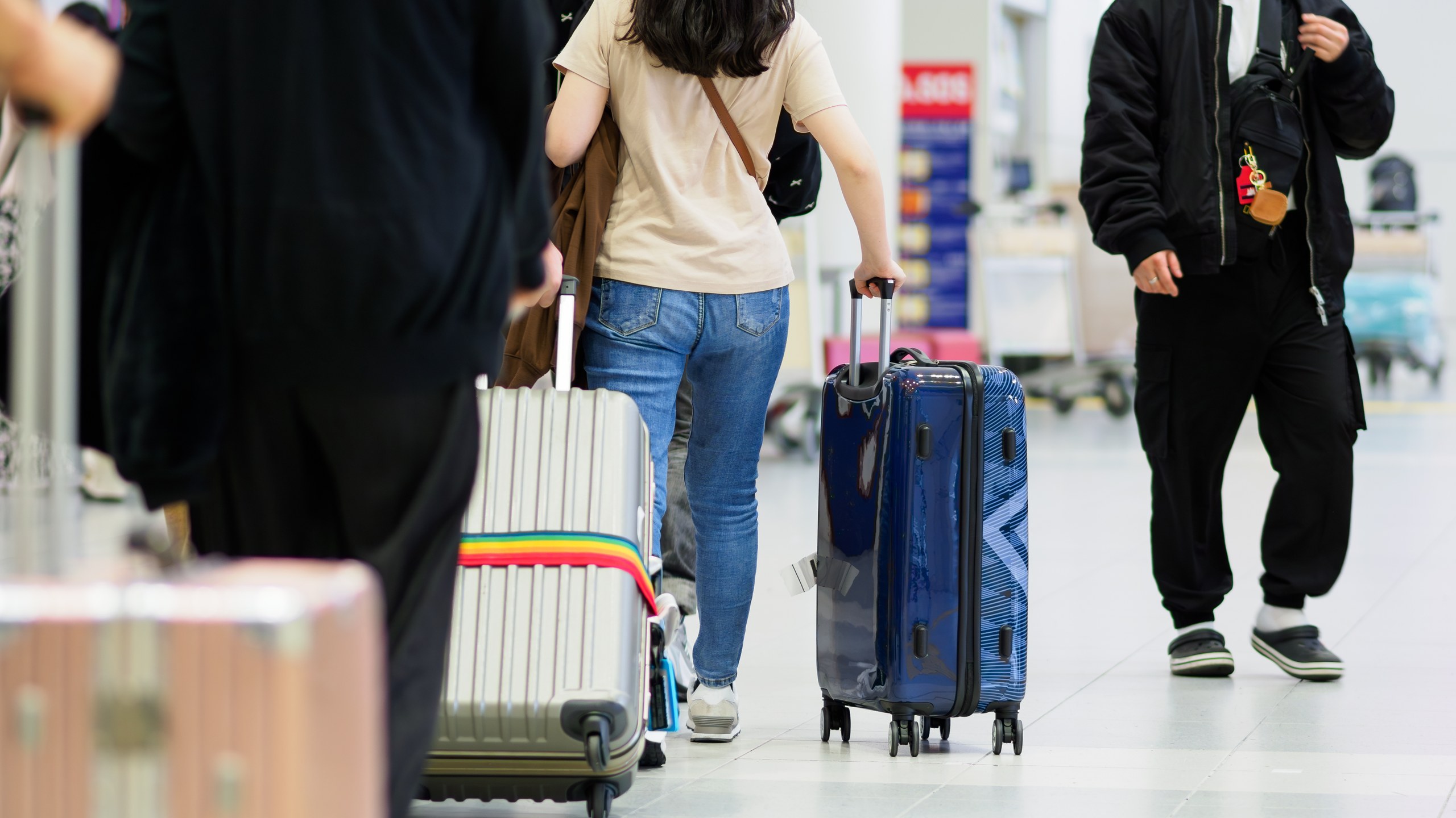 空港のロビーでスーツケースを引いて歩く旅行者の後ろ姿